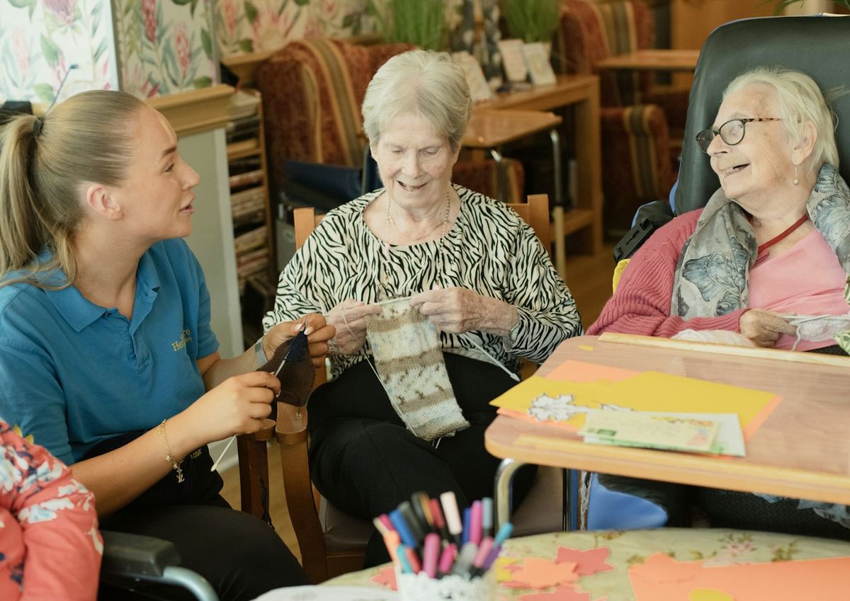 A caregiver helping two older women with knitting